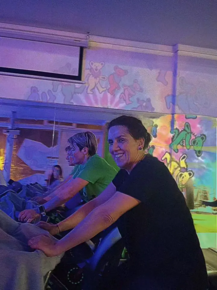 Alunas a sorrir durante uma aula de cycling, com a parede pintada ao fundo