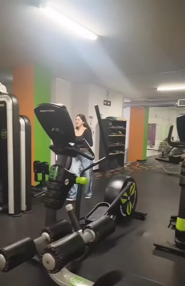 Sala de treino da Academia EquilibrioFit, com elíptica, máquinas e pilares cor de laranja e verde